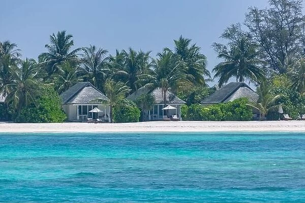 Luxury beach landscape with beach villas or bungalows with palm trees over white sand and blue sky. Summer travel and vacation view, islands beach