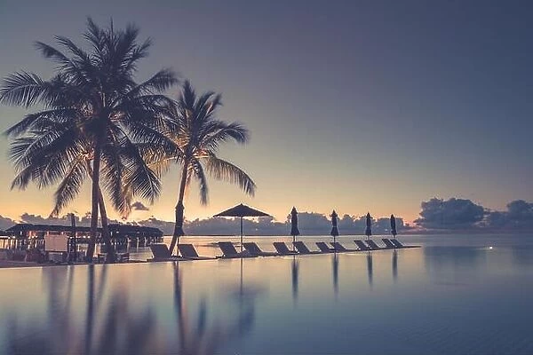 Luxury infinity beach pool in sunset time. Palm trees and calm weather on the beach. Summer vacation and holiday concept