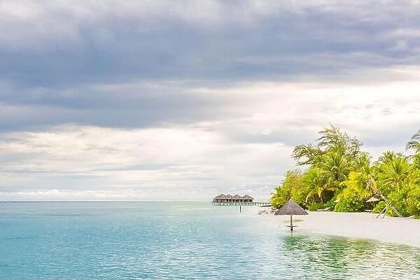 Maldives beach, overcast sky with sandy beach and water villa. Parasol in sea lagoon
