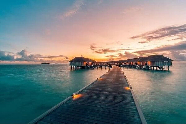Maldives island and water villas. Island in ocean, overwater villas at the time sunset with led lights and twilight sky. Luxury resort, jetty bungalow