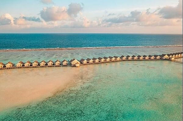 Maldives sunset paradise. Tropical aerial landscape, seascape with long pier, water villas with amazing sea sandbank lagoon beach, tropical nature
