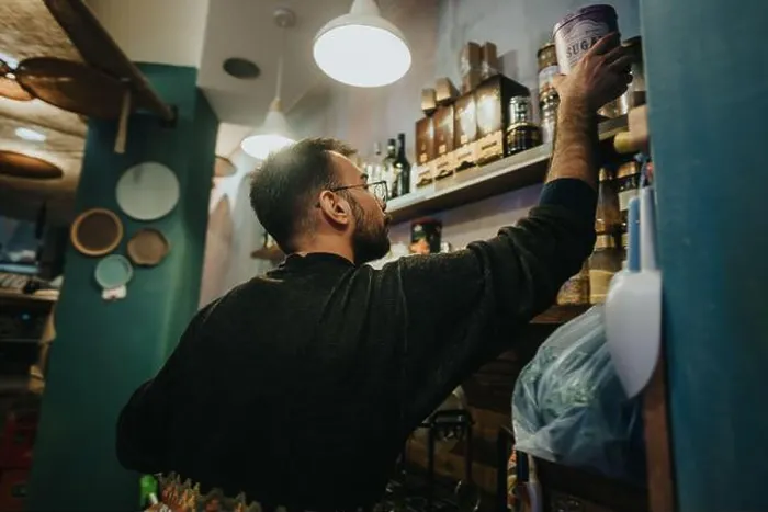 Framed Print : Man reaching for a product on a shelf in a cozy small store Framed Print : Man reaching for a product on a shelf in a cozy small store