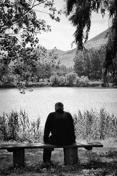 Framed Print : Man sitting on a bench overlooking the lake. Black and white image