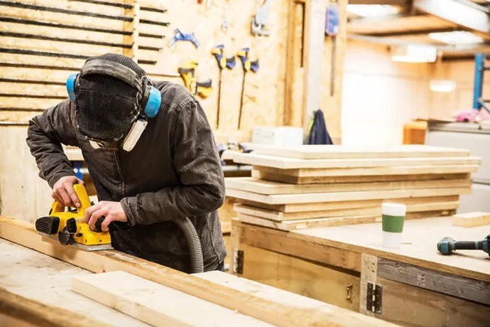 Framed Print : Man wearing ear protectors, protective goggles and dust mask standing in a warehouse, sanding planks of recycled wood Framed Print : Man wearing ear protectors, protective goggles and dust mask standing in a warehouse, sanding planks of recycled wood