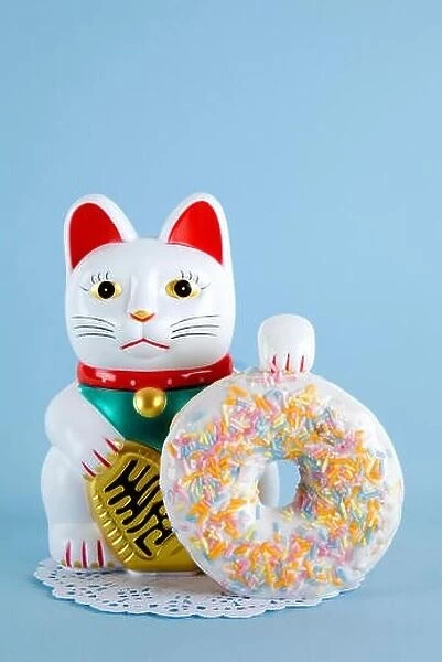 a maneki neko presenting a multicolor donuts on a doily paper and a pop colorful background. Minimal quirky color still life photography