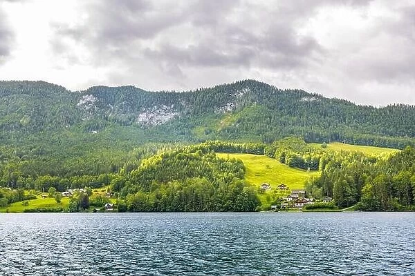 Mountain lake near the Euopean alps with green forest and field, cloudy day