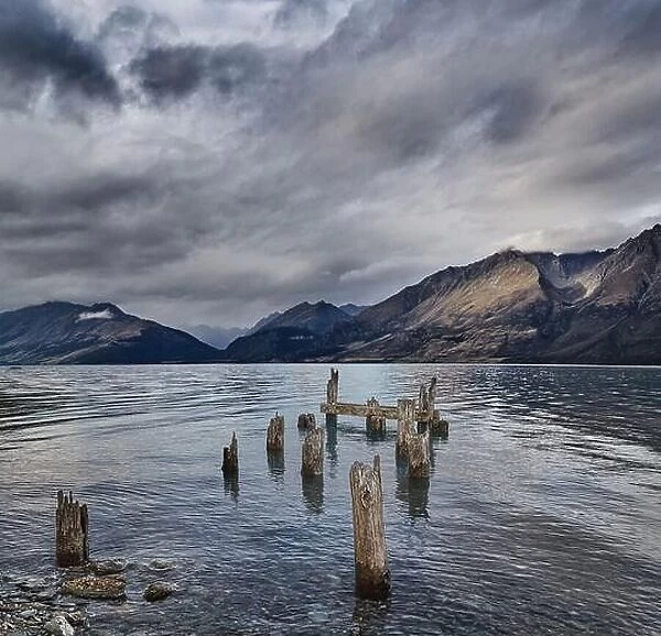 Mountain lake with remains of old wooden pier at windy cloudy morning