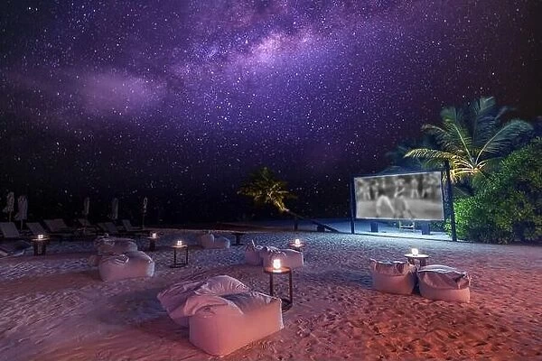 Movie night on starry tropical island beach. Amazingly calm and relaxed scenic view of outdoor cinema with the Milky Way and palm trees soft candles