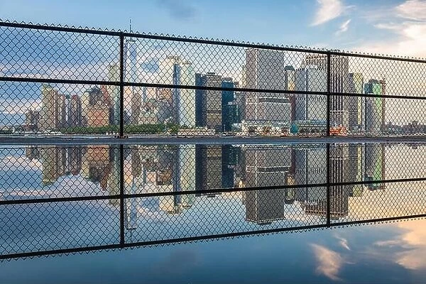 New York, New York, USA city skyline of Lower Manhattan on the New York harbor through fencing