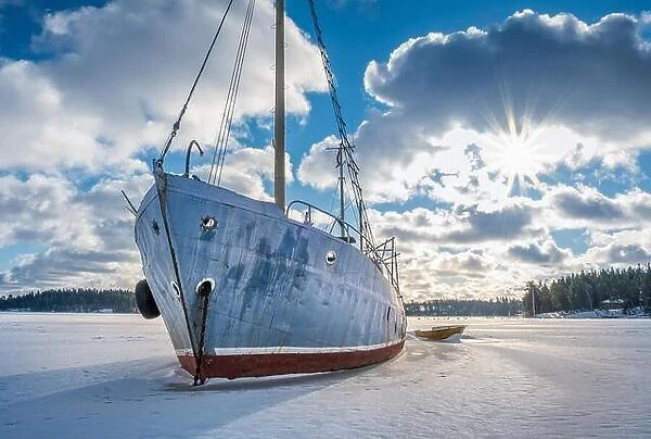 Old and broken abandoned ship on ice at sunny winter day in coastline Finland