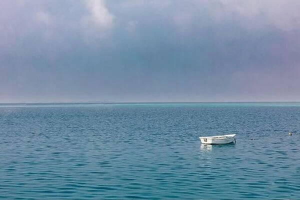 Old rowing boat marooned at sea. Lonely wooden boat, cloudy sky, calm ocean ripples with horizon