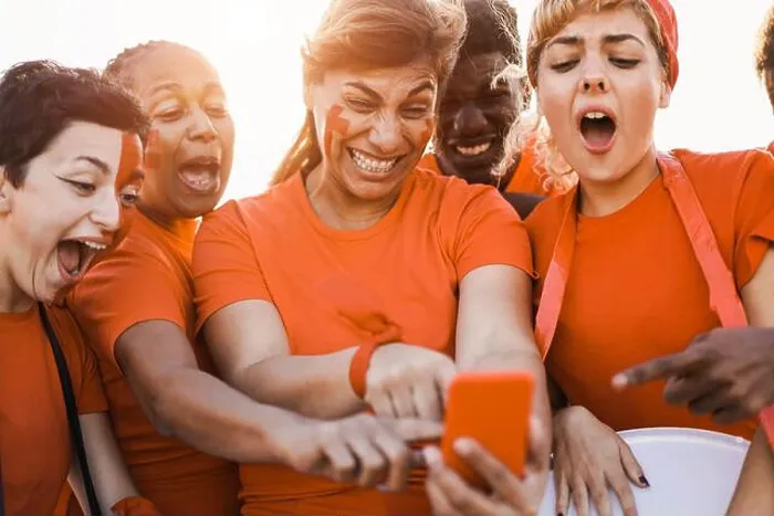 Framed Print : Orange sport supporters watching football game on mobile phone - Focus on center woman face Framed Print : Orange sport supporters watching football game on mobile phone - Focus on center woman face