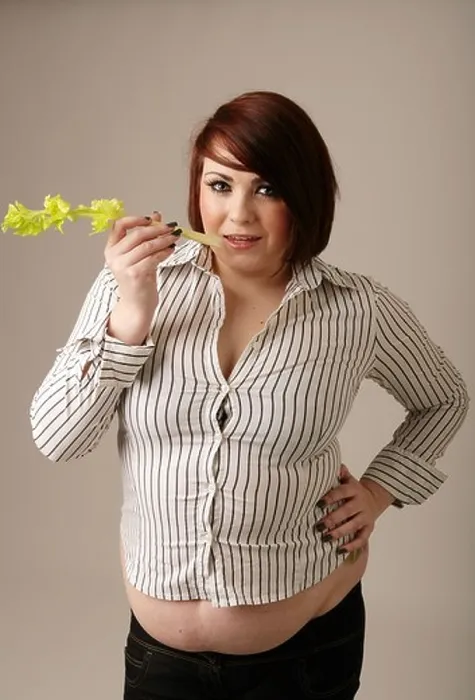 Framed Print : Overweight woman in a tight fitting shirt standing holding a stick of celery Framed Print : Overweight woman in a tight fitting shirt standing holding a stick of celery