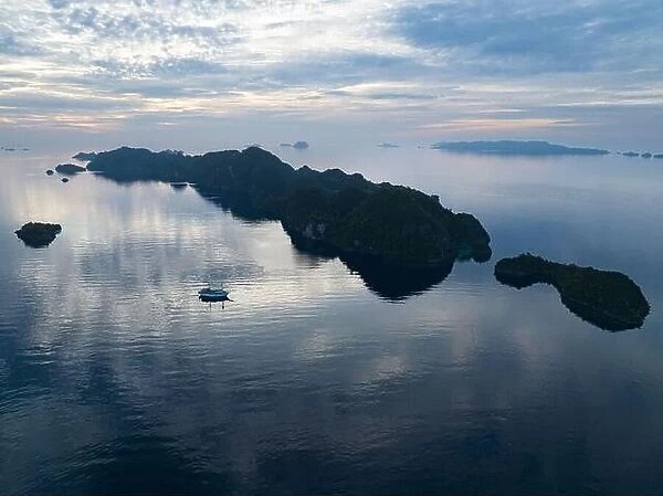 A peaceful sunrise illuminates dramatic limestone islands that rise from Raja Ampat's beautiful seascape. This area has high marine biodiversity