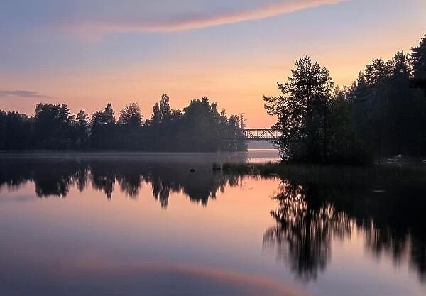 Peaceful view with sunset, lake and old bridge at summer night in Finland