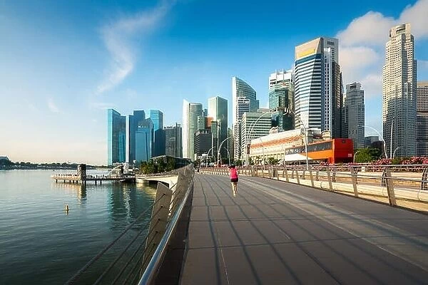 Pedestrians walk along bridge near Marina bay in Singapore with Singapore skyscraper in background