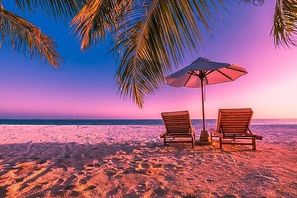 Perfect sunset beach, two sun chairs with umbrella under palm trees. Twilight sky and tranquil beach scene near the sea. Idyllic vacation and holiday