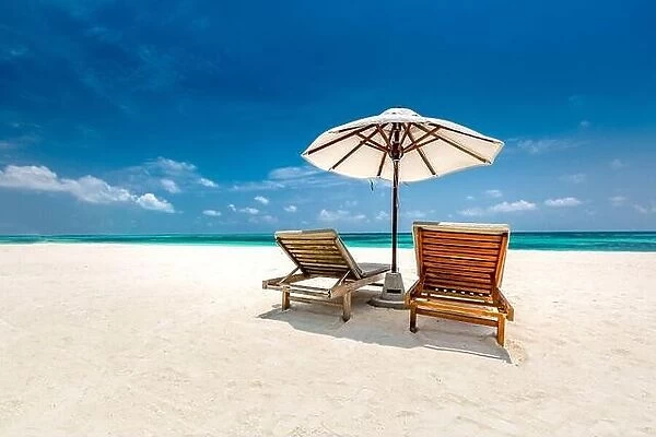 Perfect tropical beach landscape, white sand over blue sea and blue sky. Idyllic and exotic summer vacation landscape. Beach holiday, chairs, umbrella