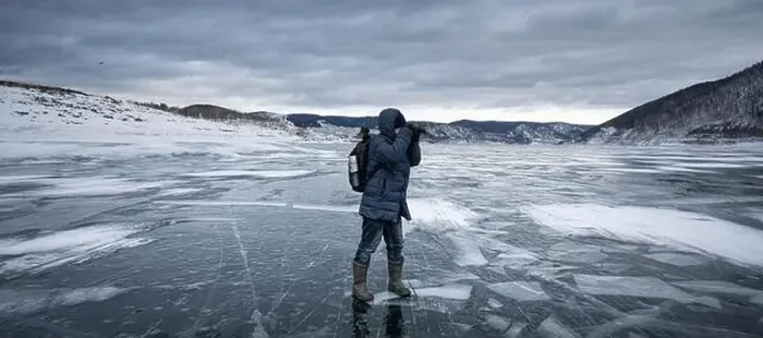 Framed Print : Person in winter gear explores and photographs the icy surface of a winter lake surrounded by snowy hills Framed Print : Person in winter gear explores and photographs the icy surface of a winter lake surrounded by snowy hills