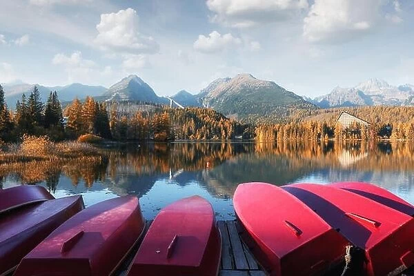 Picturesque autumn landscape with row of red wooden boats and high mountains on background. Strbske pleso lake in High Tatras National Park, Slovakia