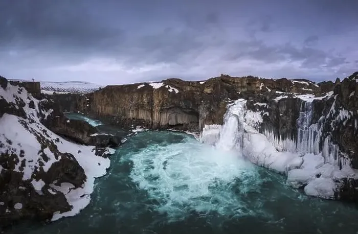 Framed Print : Picturesque drone view of Aldeyjarfoss waterfall falling from rough snowy cliff against cloudy evening sky in winter in