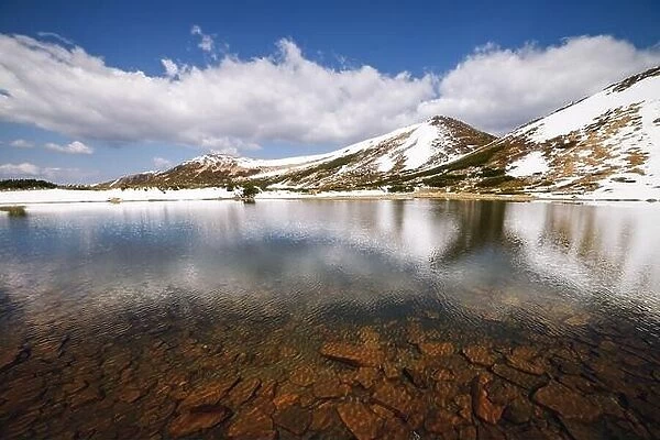 Picturesque spring landscape with snowy hills and clear mountain lake under a blue sky, Carpathian mountains, Europe