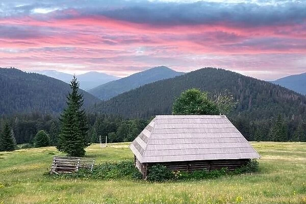 Picturesque summer meadow with old wooden house and purple sunset sky in the Carpathian mountains, Ukraine. Landscape photography