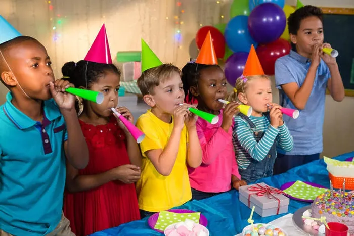 Framed Print : Playful children blowing party horns while standing by table during birthday party Framed Print : Playful children blowing party horns while standing by table during birthday party
