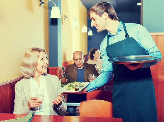 Framed Print : Positive waiter bringing order to happy smiling mature female in restaurant Framed Print : Positive waiter bringing order to happy smiling mature female in restaurant