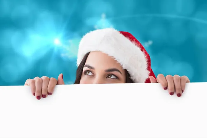 Framed Print : Pretty brunette in santa hat showing white poster against blurred christmas background Framed Print : Pretty brunette in santa hat showing white poster against blurred christmas background