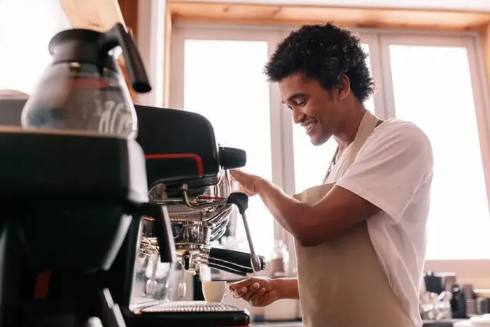 Framed Print : Professional barista holding cup on the coffee machine. Young man making coffee with an espresso coffee machine at cafe
