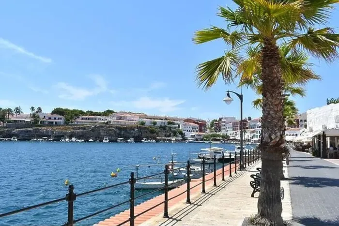 Framed Print : promenade in a village on the island of Menorca in summer sunshine, with boats and palm trees lining the road Framed Print : promenade in a village on the island of Menorca in summer sunshine, with boats and palm trees lining the road