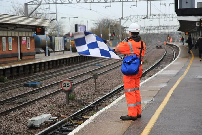 Framed Print : Railway worker wearing high visibility orange clothing holds blue and white checkered safety flag
