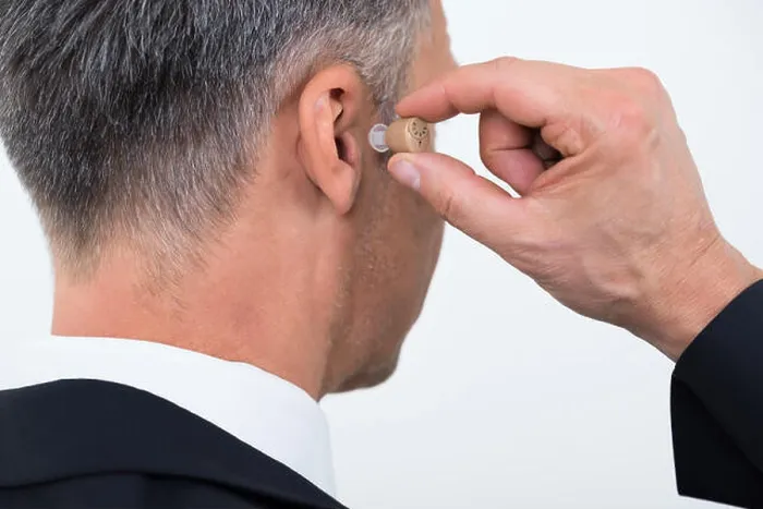 Framed Print : Rear view of businessman inserting hearing aid in ear over white background Framed Print : Rear view of businessman inserting hearing aid in ear over white background