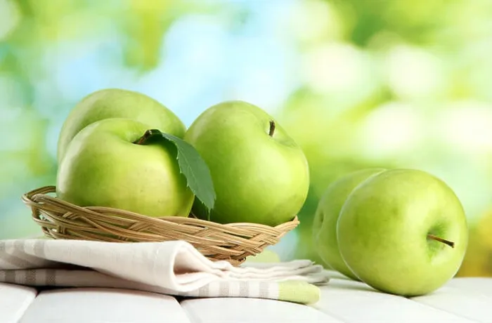 Framed Print : Ripe green apples with leaves in basket, on wooden table, on green background Framed Print : Ripe green apples with leaves in basket, on wooden table, on green background