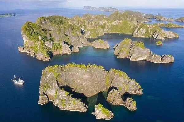 Rock islands, composed of limestone, rise from the tropical seascape in Raja Ampat, Indonesia. These islands are ancient uplifted coral reefs
