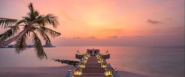Romantic dinner on the beach with sunset, candles with palm leaves and sunset sky and sea. Amazing view, honeymoon or anniversary dinner landscape