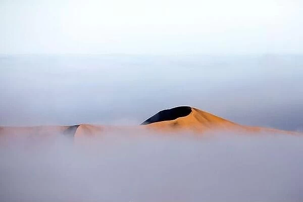 A sand dune rises above the fog line in Sossusvlei, Namibia