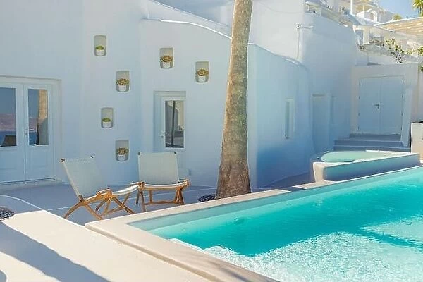 Santorini island, Greece. Luxury summer travel and vacation landscape. Swimming pool with white architecture, two chairs under palm tree. Greek style