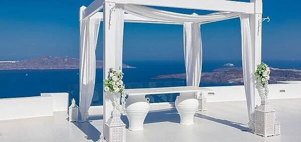 Santorini Island, Greece. Wedding decoration on a popular couple destination. Elegant wedding arch with white flowers, vases on background of blue sea