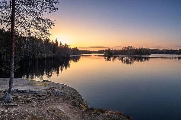 Scenic landscape with sunset, peaceful lake and tree roots at calm spring evening in Finland