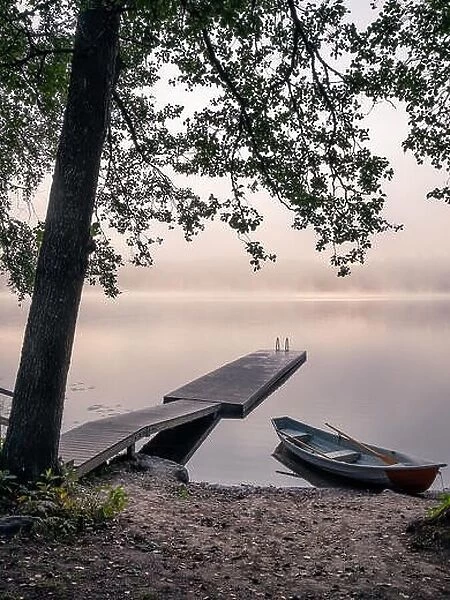 Scenic landscape view with tranquil lake, idyllic pier and boats at foggy summer morning in Finland