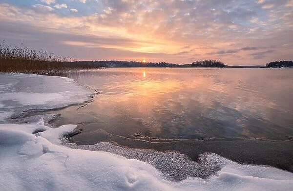 Scenic winter landscape with frozen lake and sunset at evening time in Finland