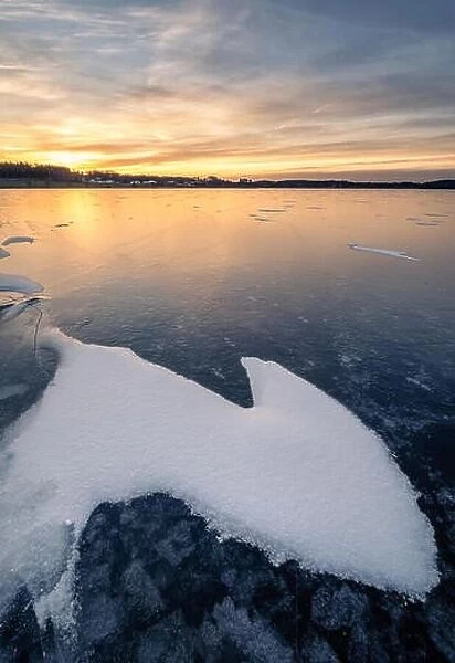 Scenic winter landscape with frozen lake and water at evening sunset in Finland
