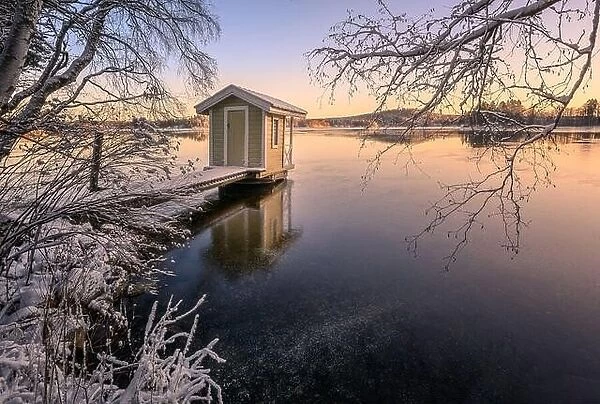 Scenic winter landscape with sunset and cozy cottage at icy and peaceful lake in Finland