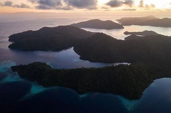Seen from above, sunrise illuminates islands in Raja Ampat, Indonesia. The islands are surrounded by healthy coral reefs and high marine biodiversity