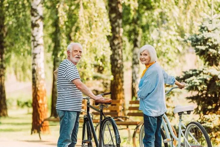 Framed Print : Senior couple smiling at camera while standing near bicycles in park Framed Print : Senior couple smiling at camera while standing near bicycles in park