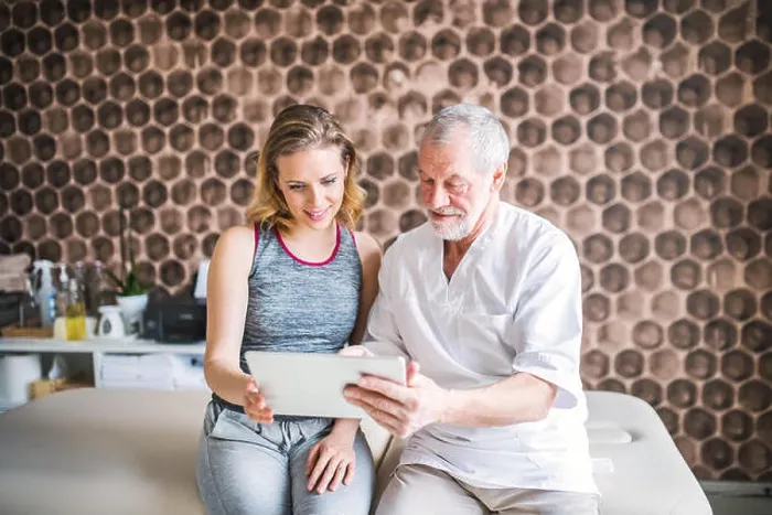 Framed Print : Senior male physiotherapist and young woman with tablet sitting Framed Print : Senior male physiotherapist and young woman with tablet sitting