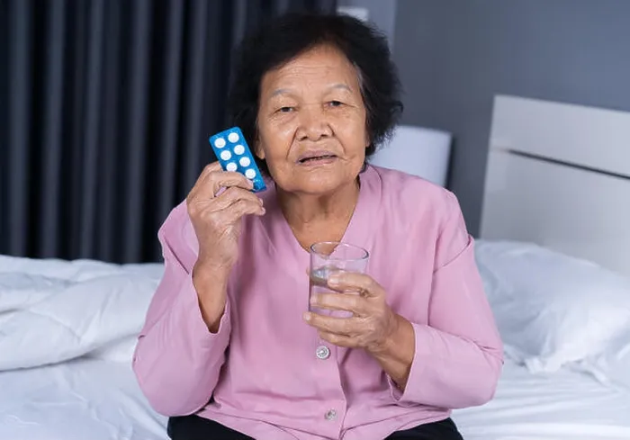 Framed Print : senior woman taking pill with glass of water in a bed