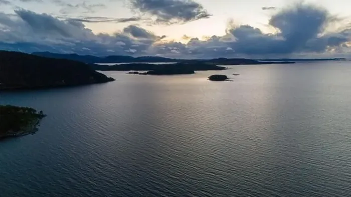 Framed Print : A serene aerial view of a large fjord with small islands and distant hills under a cloudy sky at dusk Framed Print : A serene aerial view of a large fjord with small islands and distant hills under a cloudy sky at dusk